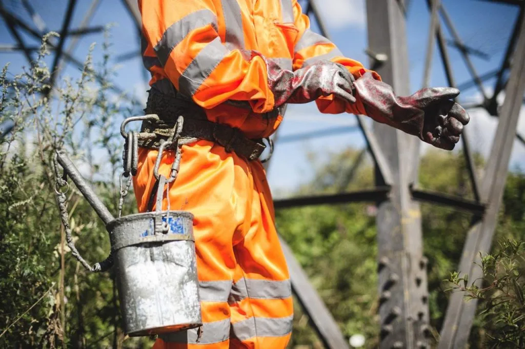 CLC contractor wearing high-visibility protective gear and gloves, preparing for maintenance work on a transmission pylon.