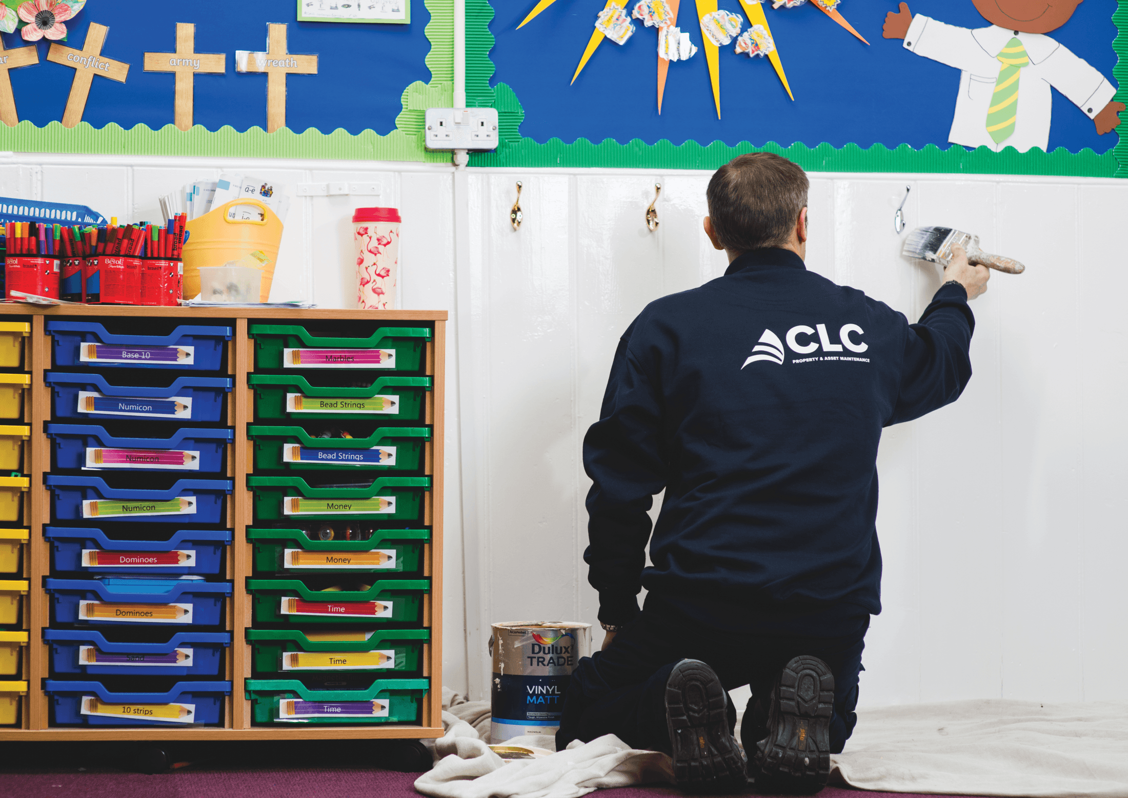CLC contractor painting a classroom wall in a school, wearing a branded CLC uniform.