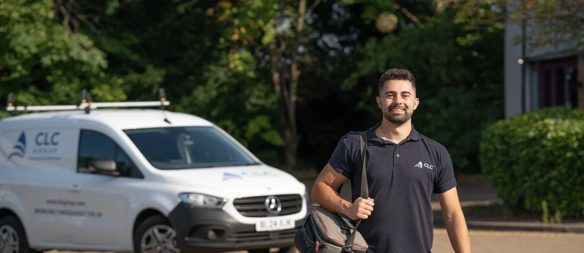 CLC contractor smiling while carrying a work bag, with a branded CLC van parked in the background.
