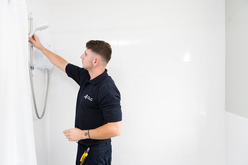 Operative in dark blue uniform installing a shower in a white tiled wet room