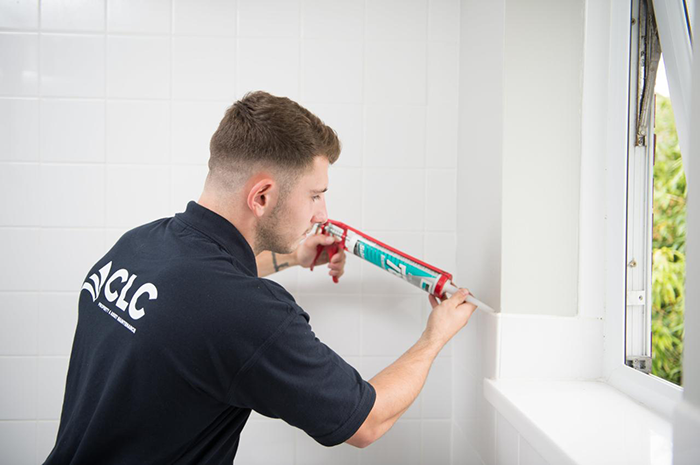 operative in blue uniform applying seal to newly installed white tiled bathroom